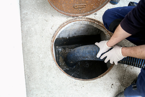 Emptying a household septic tank on a street. Unrecognizable Caucasian male manual worker cleaning sludge and mud from a sewage system.