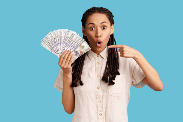 istock Woman holding dollar banknotes, pointing at cash, looking at camera with shocked expression. 1390496746