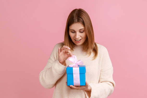 istock Positive blond woman unpacking present box, looking at her gift, pulling ribbon, excited expression. 1390497293