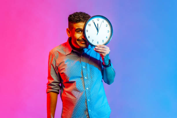 istock Man standing covering half of face with big wall clock, looking at camera with positive expression. 1390497728