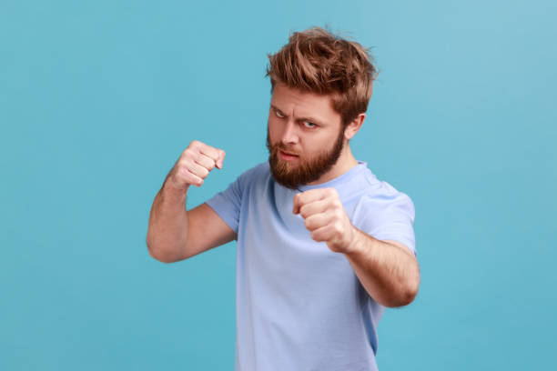 mężczyzna w niebieskiej koszulce stojący z pięściami bokserskimi i gotowy do ataku lub obrony, wygląda ze wściekłą twarzą - punching young adult boxer boxing zdjęcia i obrazy z banku zdjęć