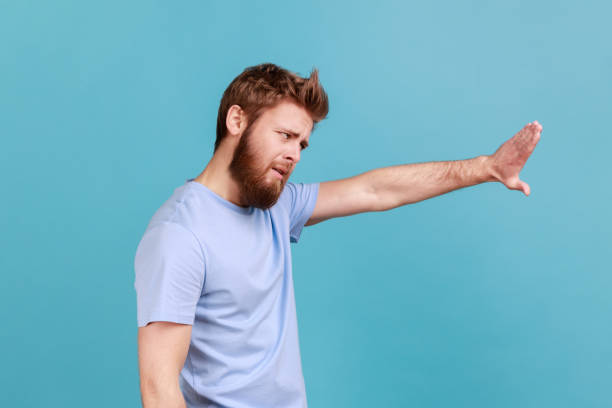 istock Side view of man showing stop sign, standing with frowning face and bossy expression, avoid danger. 1390497911