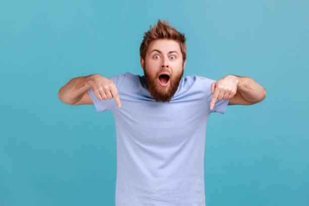 istock Man pointing down and looking at camera, showing place for idea presentation, expressing surprise. 1390497917