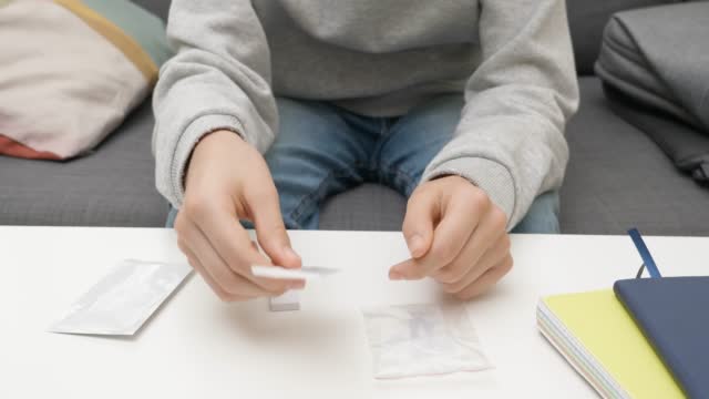 Teenage boy hands unpacking Covid-19 rapid antigen self test kit at home. Kid preparing test kit to self-test before school lesson