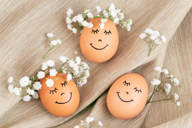 istock Three happy Easter eggs with cute faces in floral wreath crowns on brown burlap background. 1390505526