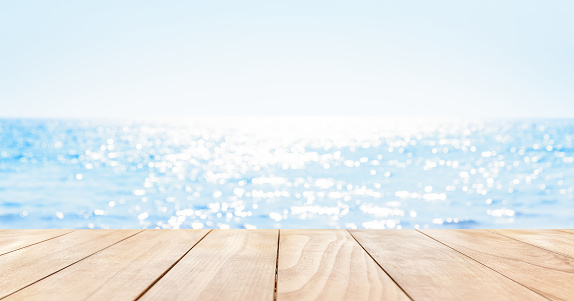 Wooden table top on blue summer sparking sea water with bokeh light. Blur shiny sea water and summer sky background.