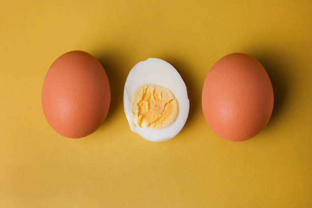 istock Two whole brown eggs and a boiled egg with yolk cut in half on an isolated light yellow background 1390505600