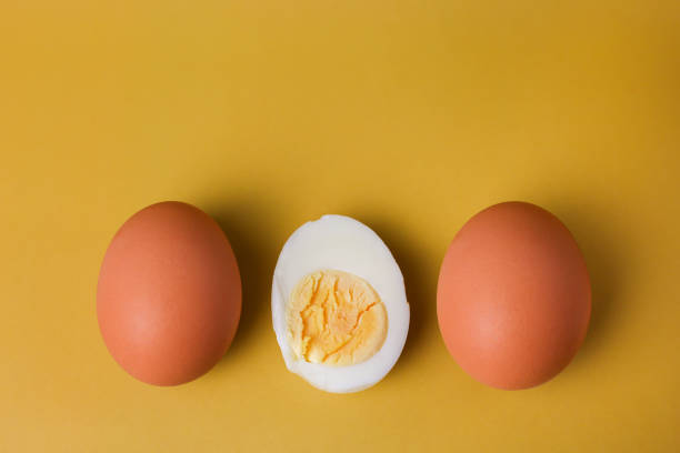 istock Two whole brown eggs and a boiled egg with yolk cut in half on an isolated light yellow background 1390505627