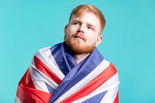 Male portrait of man at the studio with British flag of Great Britain. Color background, concept photography for England and English culture. Person is smiling and wear t-shirt.