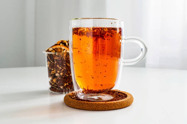 Rooibos tea in a transparent thermos mug on the table close-up. Visual for tea sample. Method of brewing and storage. Welding in a transparent teapot. Tea color, brewed citrus.