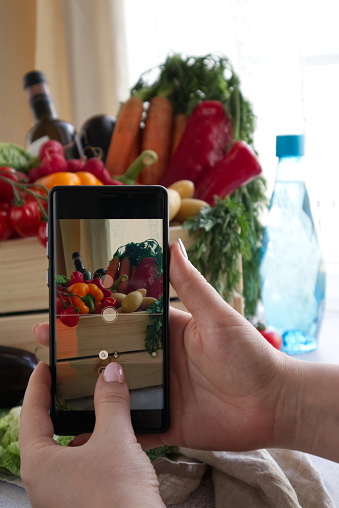 Women's hands take pictures on a smartphone of a box with fresh products prepared for delivery
