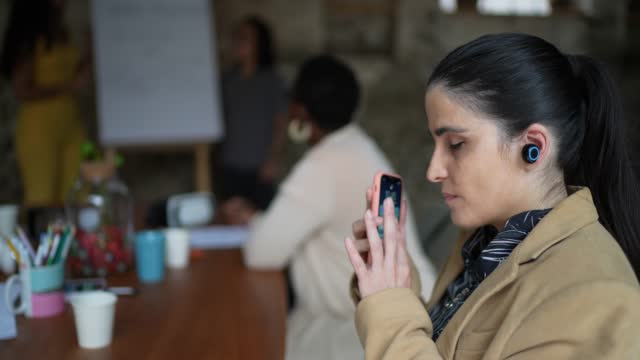 Visually impaired businesswoman using smartphone and earphones during a business meeting