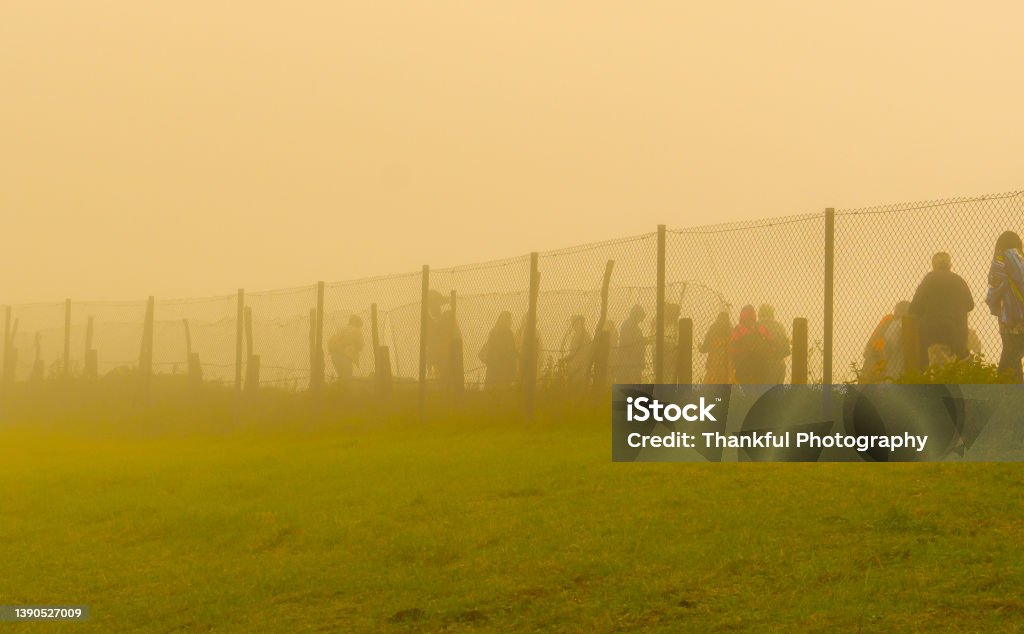 Refugees walk to the border behind the wire in a cold day under fog. Refugee Stock Photo