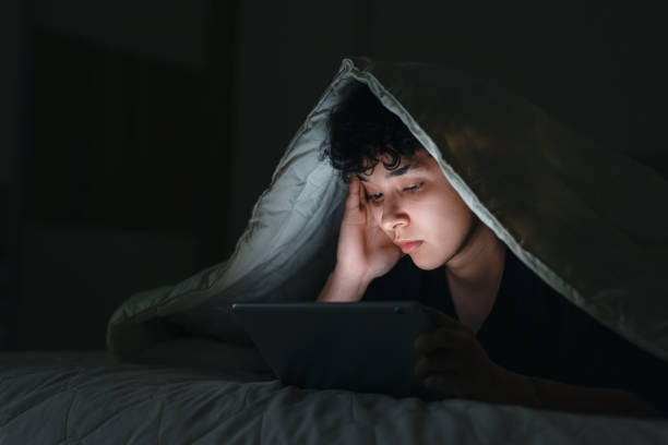 Teenage girl using smartphone in bed late at night with sad facial expression stock photo