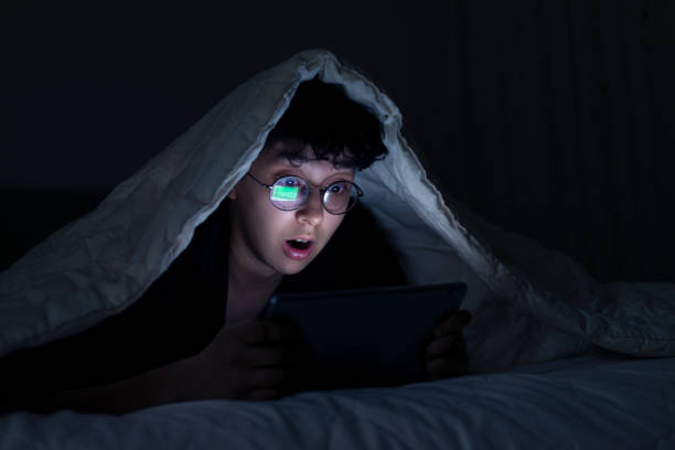 Cute girl watching video on phone with shocked facial expression in bed at night stock photo