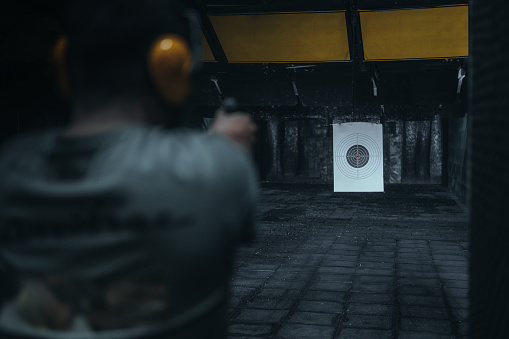 Young man practice gun shoot on target. Horizontal composition.