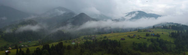 fog and rain in the carpathian mountains. mountain village dzembronya in the carpathian mountains, ukraine. panoramic photo of mystical mountain landscape. - eastern europe mountain range mountain village imagens e fotografias de stock