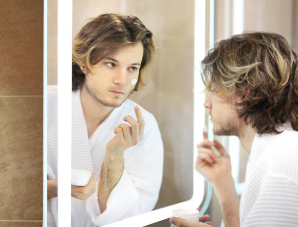 istock young man looking in the mirror,combing his hair,looking at problems on face. 1390531806