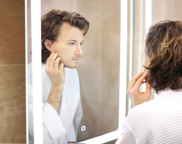istock young man looking in the mirror,combing his hair,looking at problems on face. 1390531817