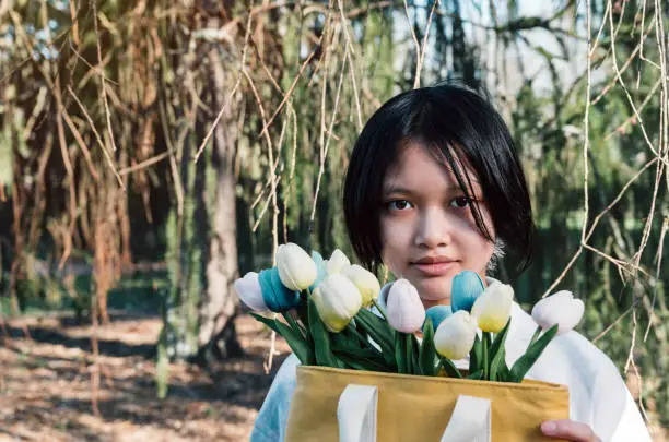 Portrait of teenage Asian girl holding bouquet of tulips flowers in bag. copy space.