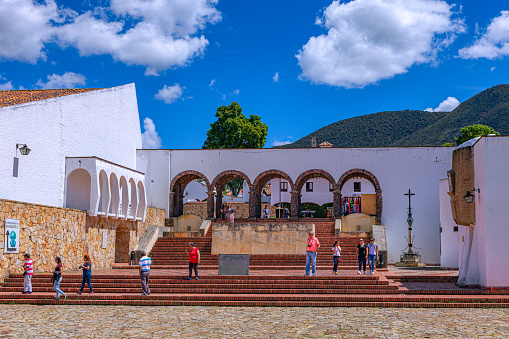 Guatavita, Colombia - January 21, 2017: The view from the main town square in Guatavita, in the Cundinamarca department of the South American country of Colombia, looking to the main entrance to the square. There are some local Colombian tourists on the square. It does not have vehicular access. The altitude is about 8,660 feet above mean sea level. In the background are the Andes mountains. Photo shot in the afternoon sunlight;  horizontal format. Copy space.