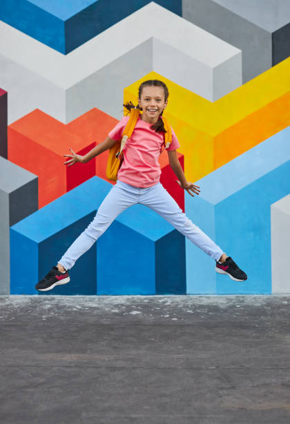 istock Merry schoolgirl jumping near graffiti wall 1390551465