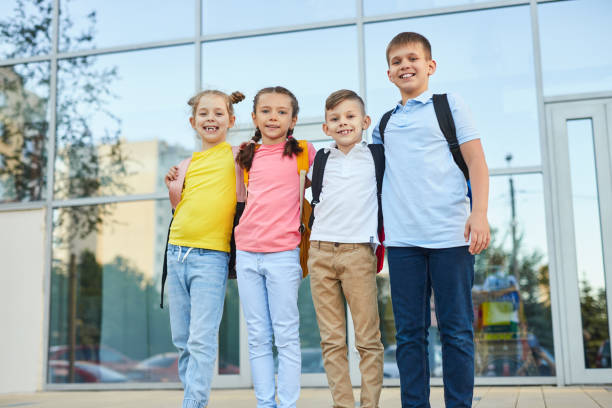 istock Smiling kids with backpacks standing near modern building 1390551535
