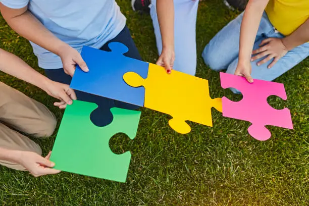 From above anonymous children connecting pieces of colorful jigsaw puzzle while sitting on grass in summer