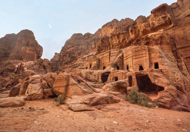 ruines d’habitation simples - des trous en forme de grotte dans un mur de pierre, lune au-dessus des montagnes - comme on le voit à petra, jordanie - petra ancient civilization jordan cave photos et images de collection