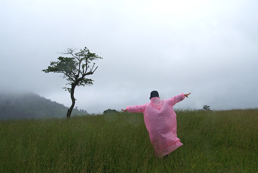 Tourists wearing pink raincoats stand with their arms out in the grass on a rainy day.