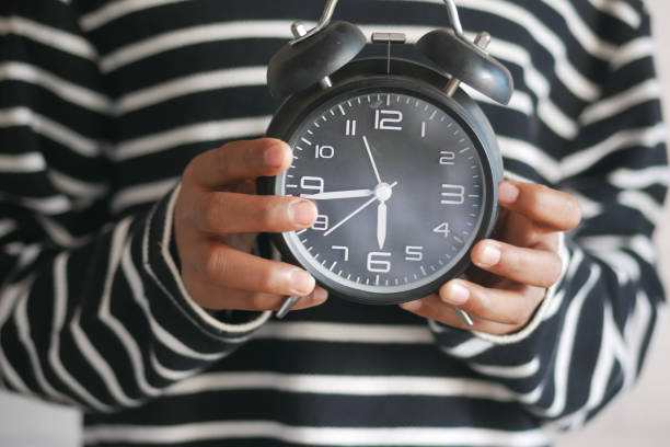 istock person hand holding alarm clock white background , 1390567652