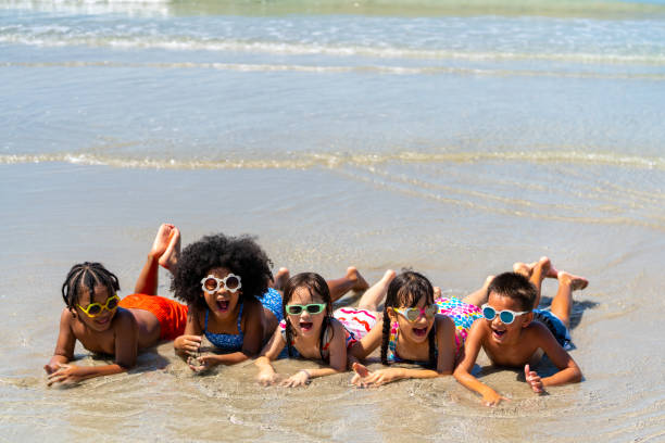 group of diversity children lying and playing together on the beach in summer vacation at the sea - summer swimming beach vacations imagens e fotografias de stock