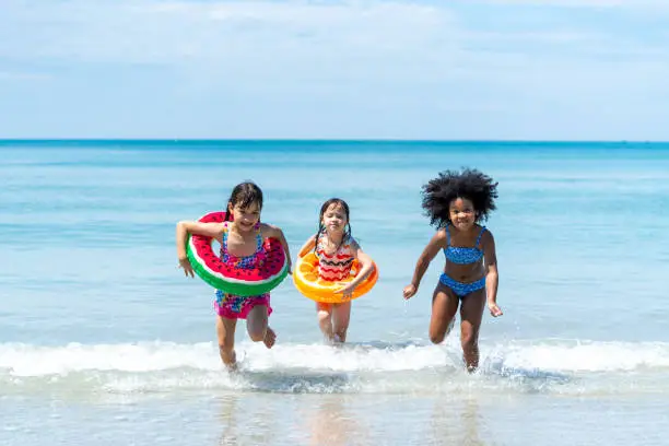 Photo of Little African and Asian girl playing in sea water together at tropical beach on summer vacation