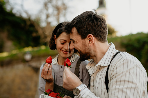Man and woman feeding each other strawberries while enjoying picnic time outdoors together. Summer holidays, people, romance concept
