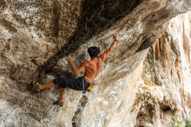 夏休みに熱帯の島の岩山に登る若いアジア人男性。 - overhanging ストックフォトと画像
