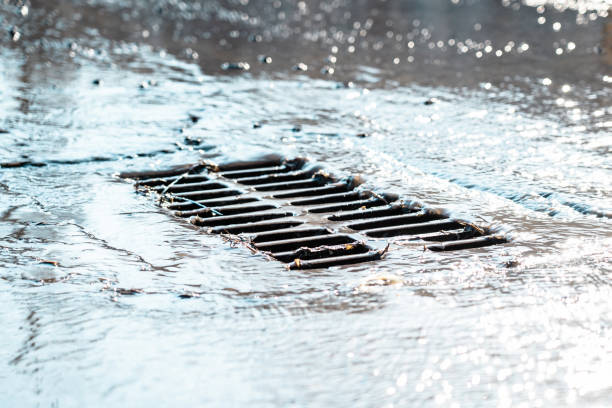 das gitter des regenkanals nach dem regen. das wasser fließt in den regenabfluss. sonnenblendung, defokussierter hintergrund - kanalisationsabflüsse stock-fotos und bilder