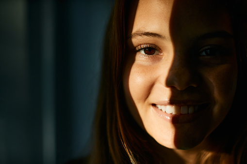 Close-up portrait of happy teenage girl with half face lit by the sun. She is looking at camera.