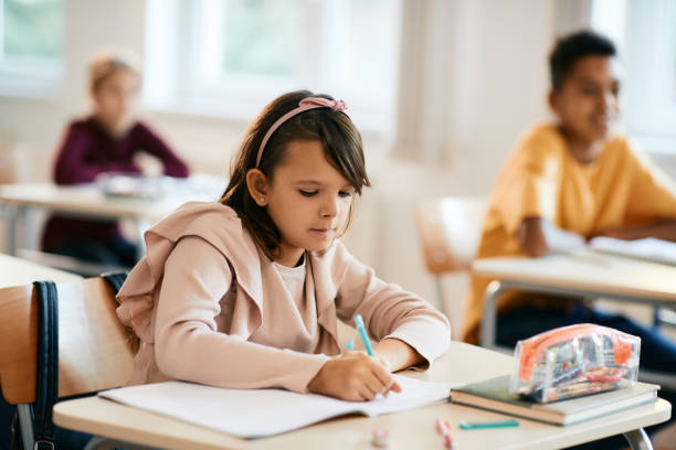istock Elementary student writing at her desk during a lesson in the classroom. 1390581406