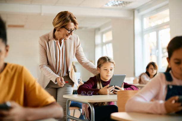 istock Senior teacher assisting schoolgirl in using digital tablet during a class at school. 1390581507
