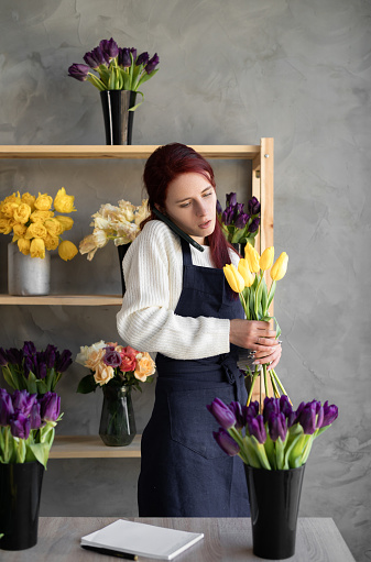 Small business. a woman florist in a flower shop near a showcase with tulips takes an order by phone. Floral design studio, scenery making. Flower delivery, ordering. copy space.