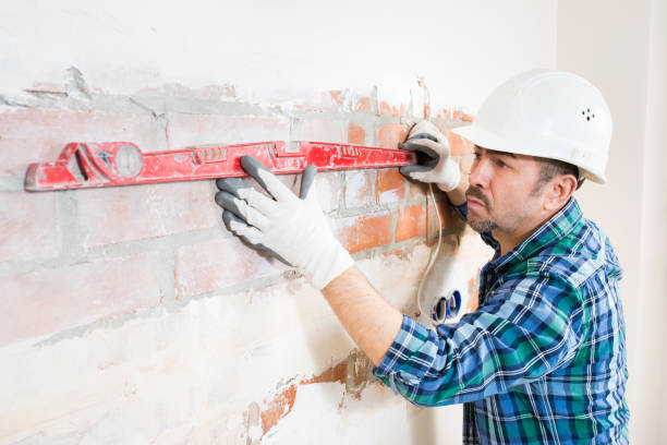 istock A builder in a safety helmet checks a flat brick wall with a building level while repairing a house, apartment, room, close-up 1390585295