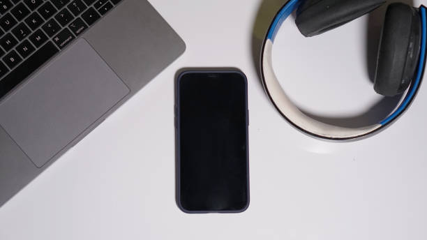 istock Smart Phone on White Table with Headphone and Laptop. Blank Screen 1390588448