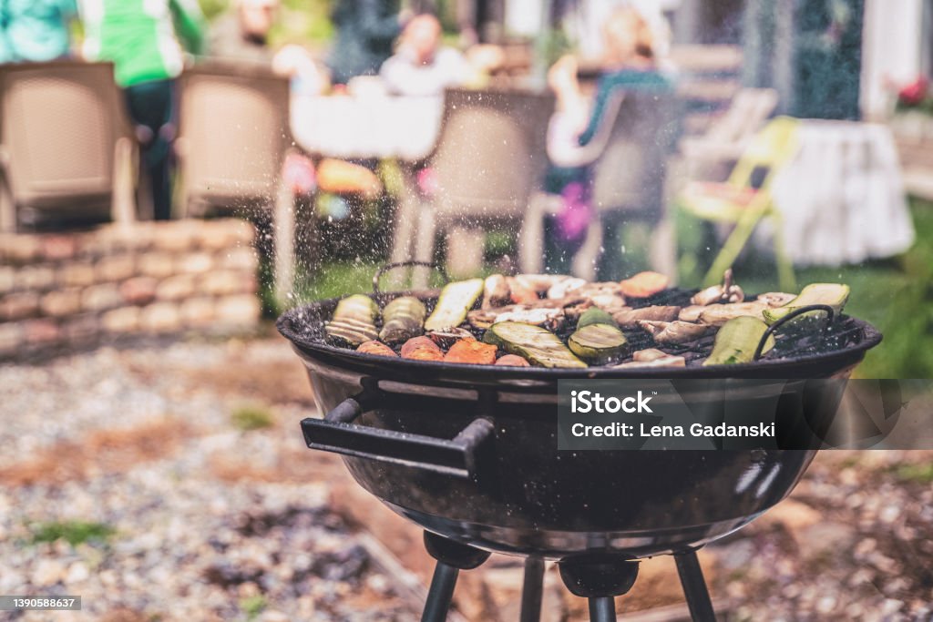 Simple round charcoal barbecue gril closeup. Simple round charcoal barbecue grill closeup. Grilling veggies outdoors for vegan party.  Ash flying around. Barbecue - Social Gathering Stock Photo