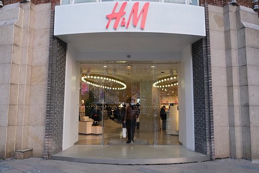 Shanghai,China-Jan.3rd 2022: facade of H&M clothing store and Chinese customer in face mask. Fast fashion clothing company
