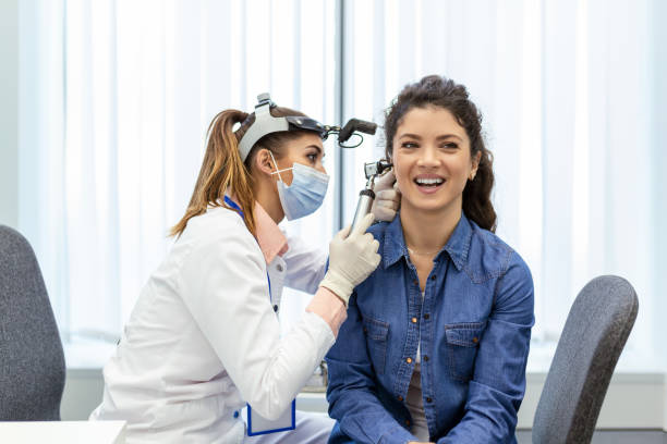 聴力試験。耳鼻咽喉科医医師は、診療所で耳鏡または耳鏡を使用して女性の耳をチェックする。耳鼻咽喉科医は手で耳を引っ張り、耳鏡のクローズアップでそれを見ます。 - 人間の耳 ストックフォトと画像