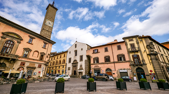 Viterbo, Italy, April 04 -- A suggestive view of Piazza del Plebiscito in the historic heart of the medieval city of Viterbo, in central Italy. On the left, the Torre Civica (Civic Tower), the highest medieval tower in the city, built in 1487. The medieval center of Viterbo, the largest in Europe with countless historic buildings, churches and villages, stands on the route of the ancient Via Francigena (French Route) which in medieval times connected the regions of France to Rome, up to the commercial ports of Puglia, in southern Italy, to reach the Holy Land through the Mediterranean. Located about 100 kilometers north of Rome along the current route of the Via Cassia, Viterbo is also known as the city of the Popes, because in the 13th century it was the Papal See for 24 years. Founded in the Etruscan era and recognized as a city with a papal document from the year 852 AD, the entire city is characterized by its stone and tuff constructions, materials abundantly present in this region of central Italy and which have always been used for the construction of houses and churches. Super wide angle image in 16:9 and high definition format.