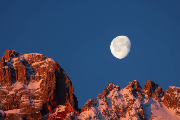A full moon rises over the snow-covered mountains in Banff National Park, Alberta, Canada in the wintertime.