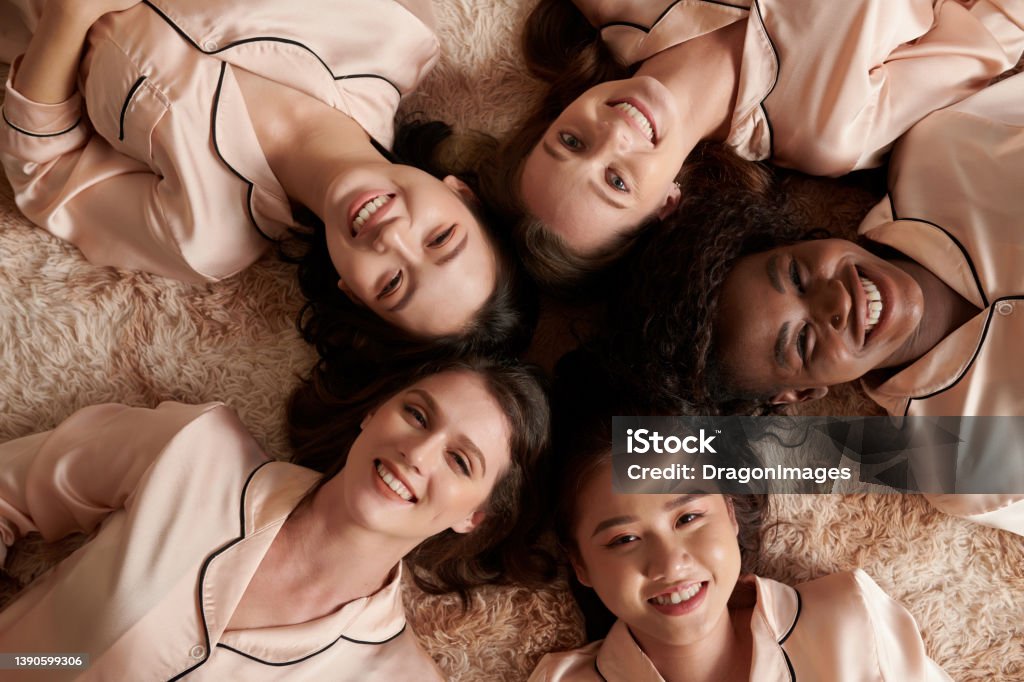 Smiling Women Lying on Floor Multi-ethnic group of smiling young women in silk pajamas lying on the floor Sorority Stock Photo