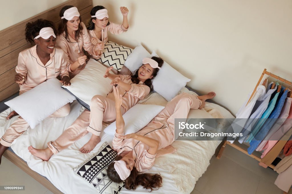 Women Enjoying Sleepover Party Group of young women in silk pajamas singing anf fooling around at sleepover party Sorority Stock Photo