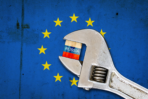 Flag of Russia on a wooden block, clamped with a wrench, against the background of the flag of the European Union. Sanctions. Country isolation. Economic blockade. Economic. Politics. Conflict.